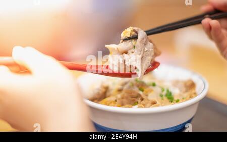 La mano usa bastoncini e cucchiaio per raccogliere gustosi tagliatelle giapponesi ramen con vegetariani e fumare in ciotola sul tavolo di legno, Foto Stock