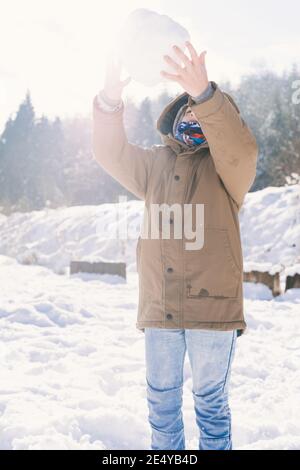 Messa a fuoco superficiale di un ragazzo in una giacca marrone cattura una grande palla di neve Foto Stock