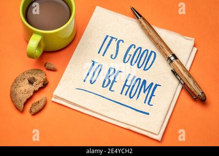 E' bene essere a casa - nota positiva. Scrivere a mano su un tovagliolo con una tazza di caffè e biscotti. Concetto di soggiorno a casa. Foto Stock