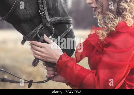 Amore per gli animali. Giovane Donna senza volto vestita in un elegante abito d'epoca, dolcemente coccolando un cavallo, stropicchiando la testa. Foto Stock