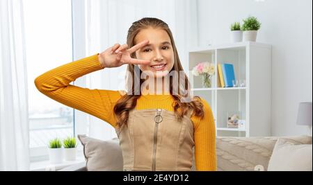 ragazza adolescente sorridente che mostra il segno di pace a casa Foto Stock