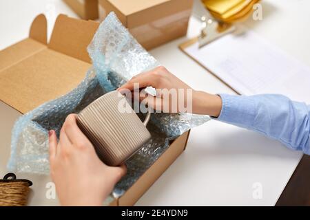 consegna la tazza di imballaggio alla scatola del pacco presso l'ufficio postale Foto Stock