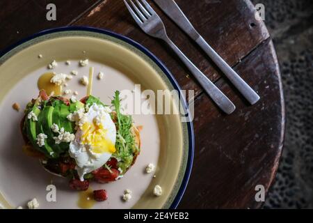 Toast all'avocado con uova in camicia, formaggio feta e fragola per un primo piano veloce Foto Stock