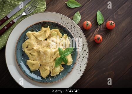 Ravioli italiani ripieni di ricotta e spinaci conditi con parmigiano grattugiato su un piatto su fondo ligneo, vista dall'alto Foto Stock
