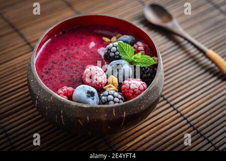 Ciotola Acai Smoothie con mirtillo, mora, lampone, muesli e semi di chia in ciotola di conchiglia di cocco Foto Stock