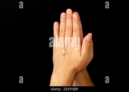 Mani giovani maschi con croce cristiana che prega a Dio a. chiesa su sfondo scuro Foto Stock