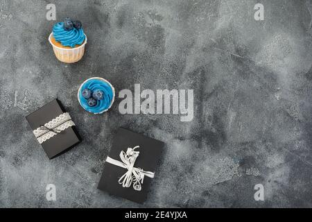 Muffin con crema blu e regalo su sfondo scuro. Disposizione piatta, vista dall'alto Foto Stock