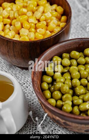 Ciotole di mais dolce bollito e piselli verdi e loro salsa su una tovaglia bianca Foto Stock