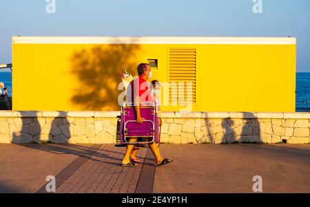 Fuengirola. Settembre 2020. Coppia ritirata con maschere passeggiate con le loro sedie da spiaggia lungo la passeggiata al tramonto. Foto Stock