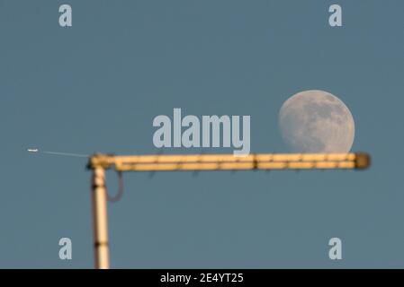 Londra, Regno Unito. 25 gennaio 2021. Regno Unito Meteo – UNA luna gibbosa al 90% si erge sopra Londra nord-occidentale in un pomeriggio limpido, giustapposta dietro un'antenna televisiva e un aereo di passaggio. Il tempo nuvoloso dovrebbe arrivare nei prossimi giorni. Credit: Stephen Chung / Alamy Live News Foto Stock