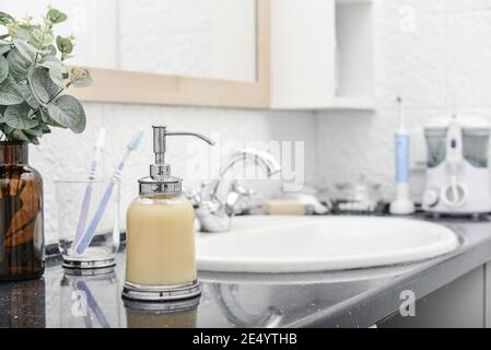 Set da bagno di vetro con dosatore per sapone liquido, spazzolini, asciugamani e sapone in bagno Foto Stock