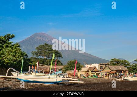 Amed spiaggia a Bali, Indonesia. Le tradizionali barche da pesca chiamate jukung sulla spiaggia di sabbia nera e il vulcano Agung sullo sfondo. Foto Stock