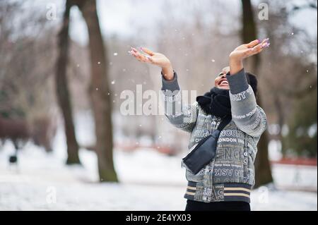 Donna africana indossare in nero sciarpa posa in inverno giorno a Europa gettare la neve in aria. Foto Stock