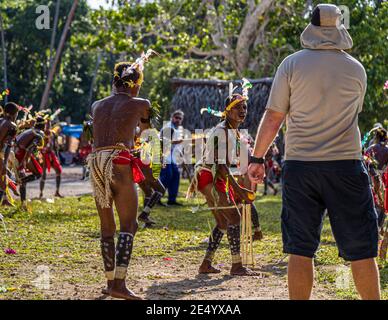 Un passeggero della nave da spedizione True North osserva due ballerini in costume davanti al wicket durante una partita di cricket in stile delle isole Trobriand a Kwebwaga, isole Trobriand, Papua Nuova Guinea, altri ballerini e un uomo con occhiali da sole sullo sfondo. Foto Stock