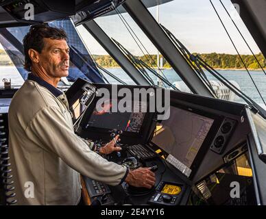 Il capitano della nave di esplorazione True North dirige dal ponte di comando, circondato da radar e monitor di cartografia, al largo della costa della Papua Nuova Guinea. Foto Stock
