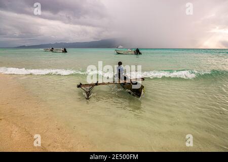 Giovani surfs locali una canoa Outrigger sulla spiaggia di Bougainville, Papua Nuova Guinea Foto Stock