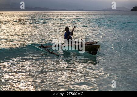 Giovani surfs locali una canoa Outrigger sulla spiaggia di Bougainville, Papua Nuova Guinea Foto Stock