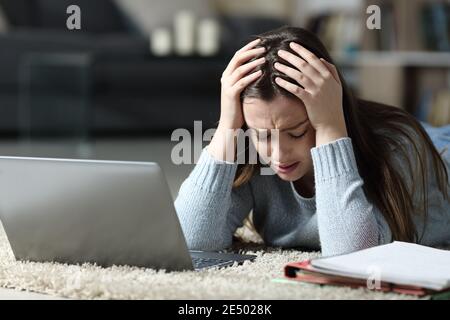 Triste studente con notebook e notebook che si lamenta di essere sdraiato sul pavimento di notte a casa Foto Stock