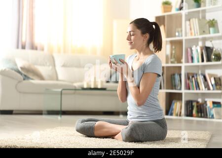 Yogi bere tè dopo esercizi di yoga seduto sul pavimento a casa Foto Stock