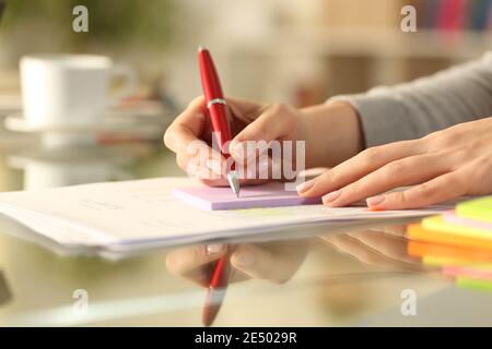 Primo piano di una mano donna che scrive su nota appiccicosa su un tavolo a casa Foto Stock