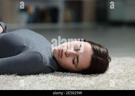 Donna triste che guarda via sdraiata su un tappeto sul piano di casa Foto Stock