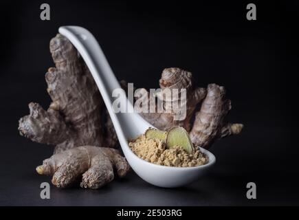 Radice di zenzero e polvere di zenzero in un cucchiaio isolato su sfondo nero, primo piano. Foto Stock