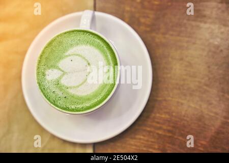 Tazza di latte matcha su sfondo di legno e un tovagliolo beige in un caffè con spazio per le copie. Foto di alta qualità Foto Stock