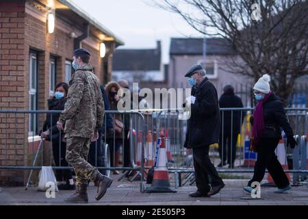 Cardiff, Galles, Regno Unito. 25 gennaio 2020. Un uomo in uniforme militare conduce una coppia anziana in prima fila per il vaccino contro il coronavirus al di fuori di un centro di immunizzazione nella zona di Splott di Cardiff. Il ministro della sanità del Galles Vaughan Gething ha dichiarato oggi che non è chiaro se sia stato raggiunto un impegno a vaccinare il 70% degli over-80 e di coloro che si trovano nelle case di cura. Credit: Mark Hawkins/Alamy Live News Foto Stock