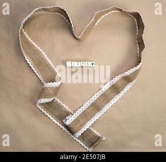 Design piatto, nastro di burlap naturale a forma di cuore con testo VEGAN scritto e carta artigianale sfondo texture, vista dall'alto, Healht, Vegan Foto Stock
