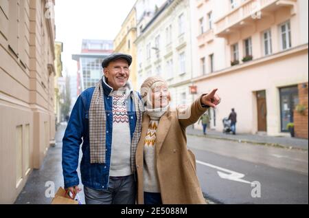 Felice coppia senior che cammina all'aperto sulla strada in città, indicando qualcosa. Foto Stock