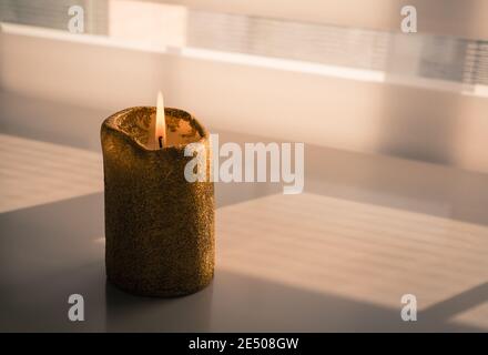 Candela che brucia su un tavolo di legno accanto ad una finestra attraverso il quale entra una debole luce notturna Foto Stock
