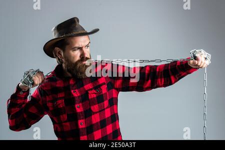 Cowboy uomo con barba e baffi tirare catena in acciaio, routine al ranch. Foto Stock
