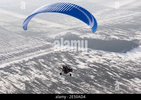 Parapendio motorizzato o buggy paramotore visto dal cielo in La Francia sorvola i campi innevati in inverno Foto Stock