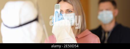 Medico in tuta protettiva che misura la temperatura delle persone in linea con termometro a infrarossi senza contatto Foto Stock