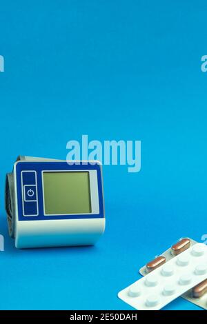 Il dispositivo per la misurazione della pressione sanguigna è realizzato su sfondo blu. Tonometro e compresse su sfondo blu con spazio per il testo Foto Stock