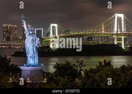 Lo skyline di Tokyo di notte, visto da Odaiba, con un ponte sospeso, una statua della replica liberty Foto Stock