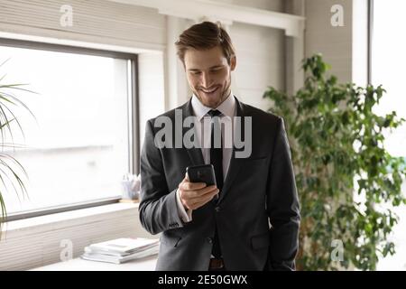 Uomo d'affari sorridente e sicuro che indossa il vestito guardando lo schermo del telefono Foto Stock