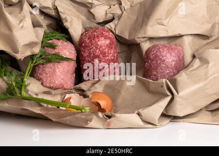 ingredienti crudi per cotolette, polpettine o palle di carne, carne tritata mista organica, uovo, cipolla, erbe, aneto su carta eco sfondo Foto Stock