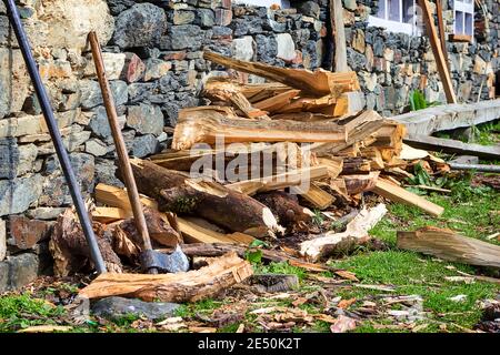 Una vecchia ascia di legno inserita in un vecchio pezzo di legno segato sullo sfondo di legna da ardere tagliata. Foto Stock