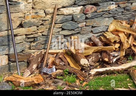 Una vecchia ascia di legno inserita in un vecchio pezzo di legno segato sullo sfondo di legna da ardere tagliata. Foto Stock