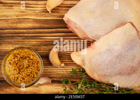 Cosce di pollo crude con rametto di timo fresco, aglio e senape su una tavola di legno marrone Foto Stock