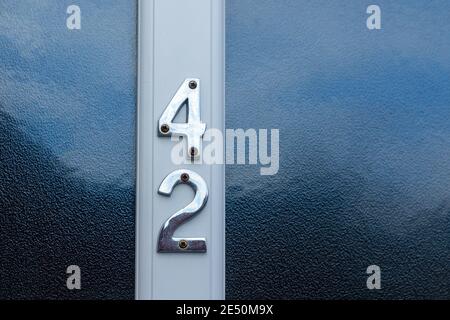 Numero 42 in cifre metalliche lucide su una porta bianca con vetro smerigliato Foto Stock