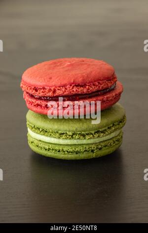 Lamponi dolci e macaroni al pistacchio isolati su sfondo di legno scuro. Pasticceria francese. Piccoli deliziosi dolci francesi. tradizionale dessert francese clos Foto Stock