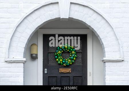 I baubles verdi formano una corona di Natale su una porta anteriore sotto un alcova Foto Stock