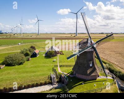 Vista aerea grandangolare di un antico mulino a vento contro grande parco eolico di turbine eoliche moderne Foto Stock