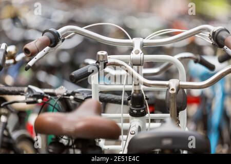 Primo piano del manubrio di un gruppo di persone parcheggiate biciclette olandesi su sfondo bokeh Foto Stock