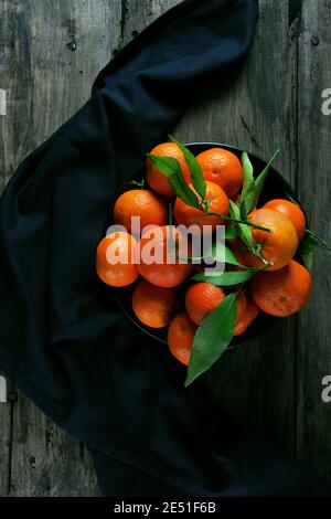 Ciotola nera con tangerini su asciugamano da cucina nero e su tavolo rustico Foto Stock