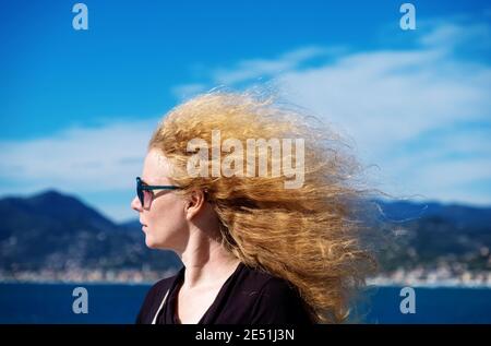 Ritratto di una bella donna matura con capelli ricci rossi in vacanza a Sestri Levante, italia al mare con capelli molto ventosi, copia spazio Foto Stock