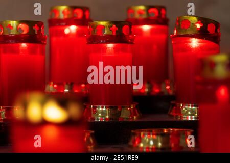 Una rastrelliera di candele rosse votive di preghiera in una chiesa italiana. Le fiamme a lume di candela in fila sono simbolo di religione silenziosa per la pace, la vita e l'anima. Foto Stock