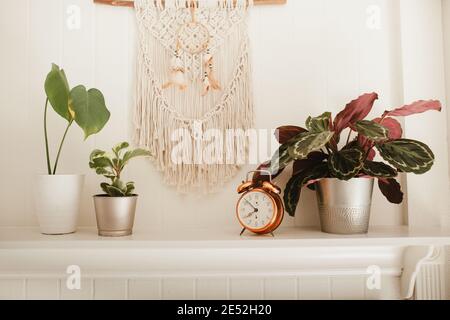 Camino in legno bianco con macrame e sogni catcher sulla parete, con piante casa e allarme rame vintage sulla mensola fuoco posto Foto Stock